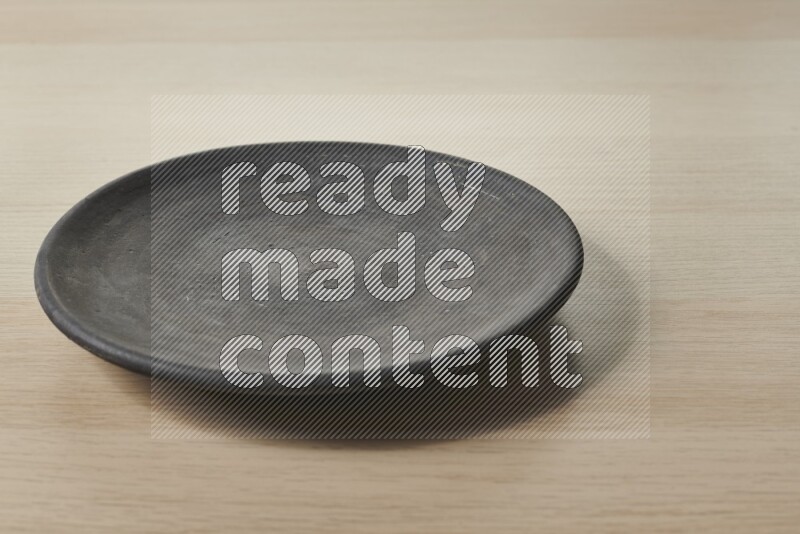 A circular black pottery plate on light wooden background