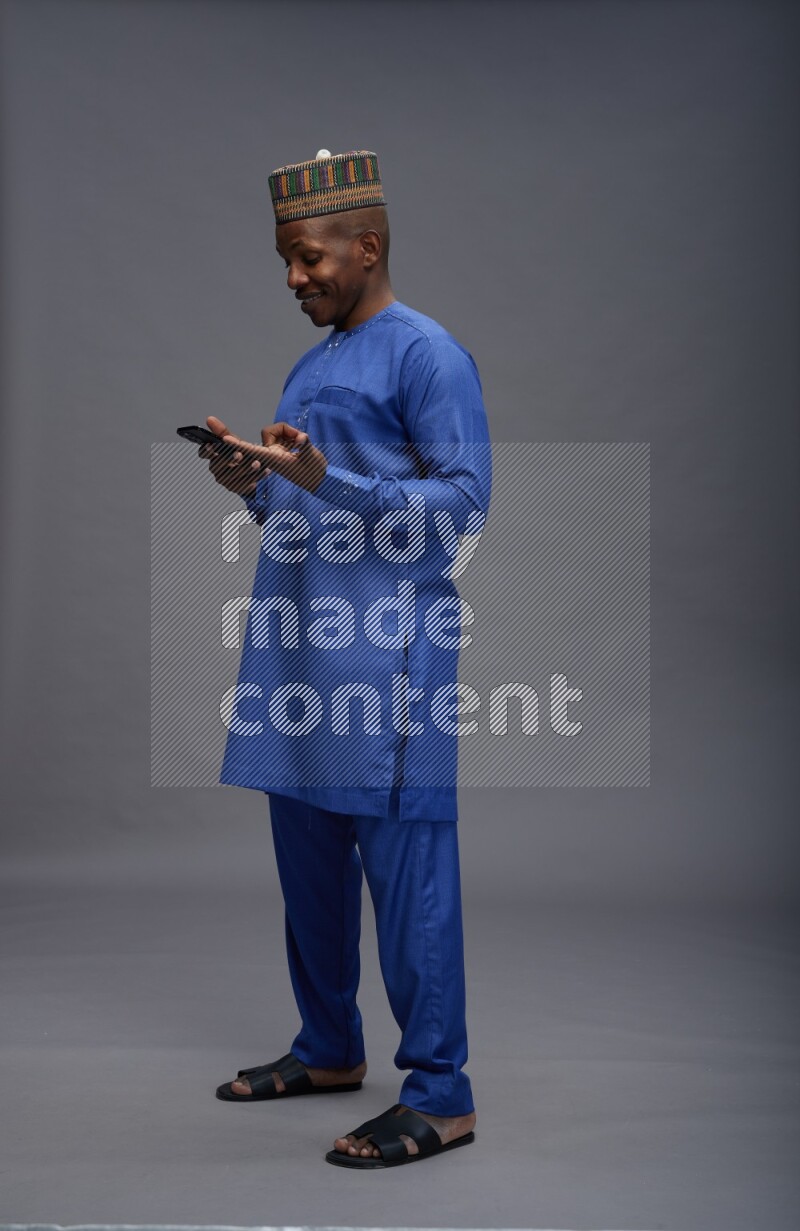 Man wearing Nigerian outfit standing texting on phone on gray background