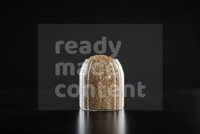 Hulled wheat in a glass jar on black background