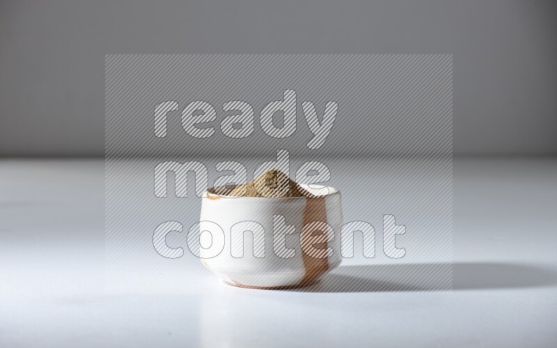 وعاء بيج ممتلئ ببودرة الكمون على خلفية بيضاء