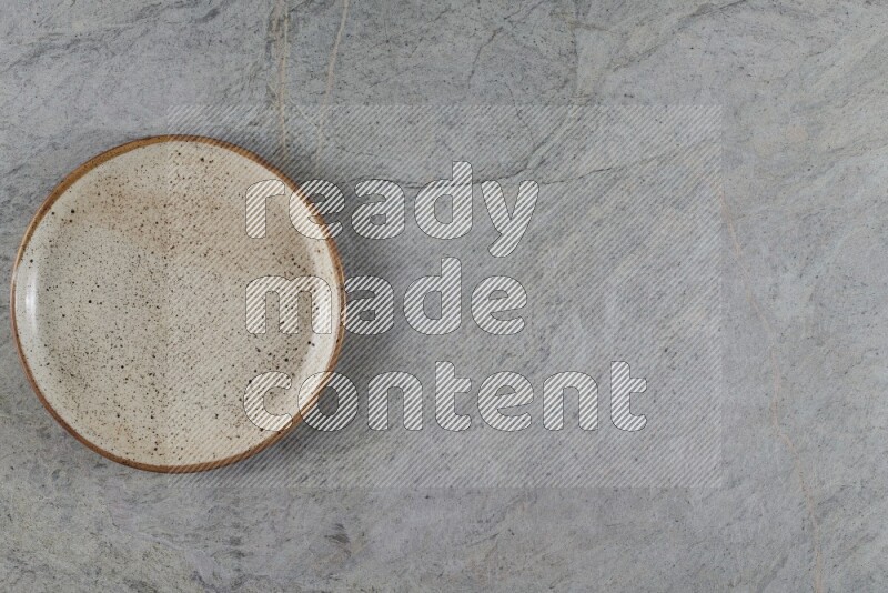 A circular beige pottery plate on grey marble background