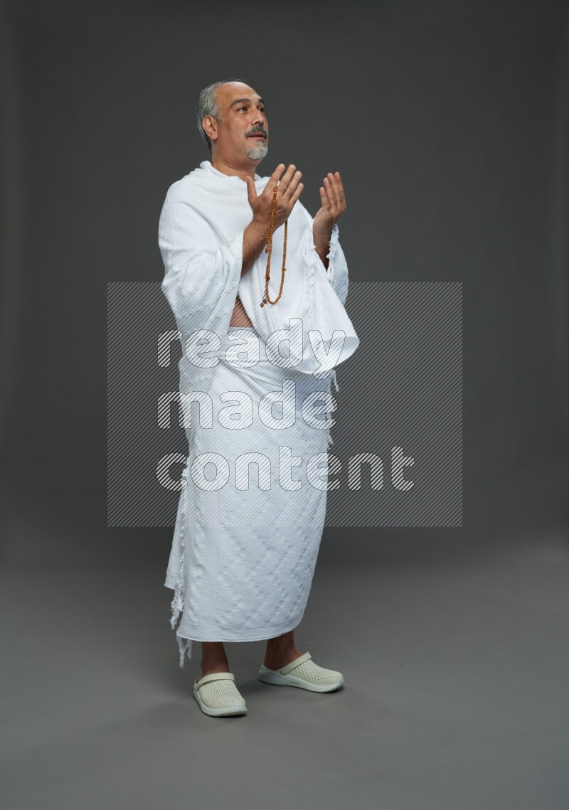 A man wearing Ehram Standing dua'a on gray background