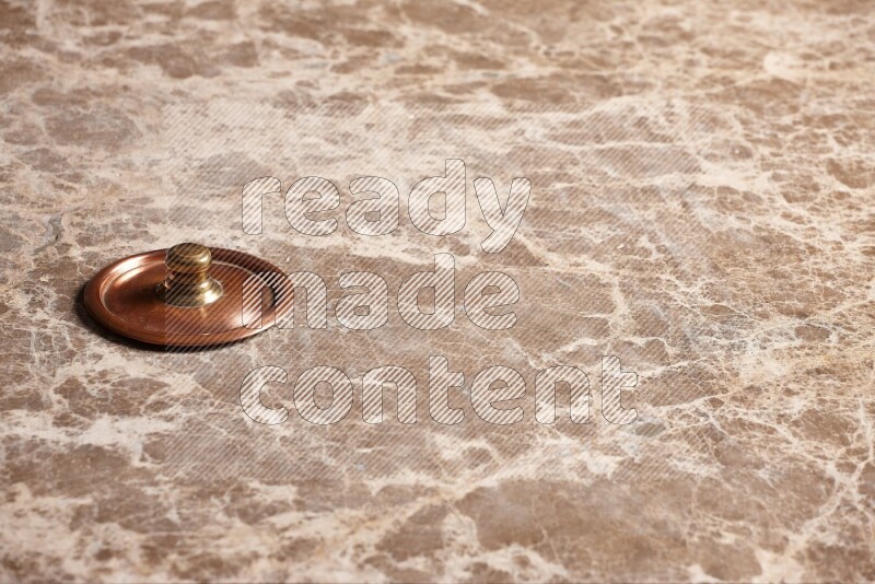 A small copper pot lid on beige marble background