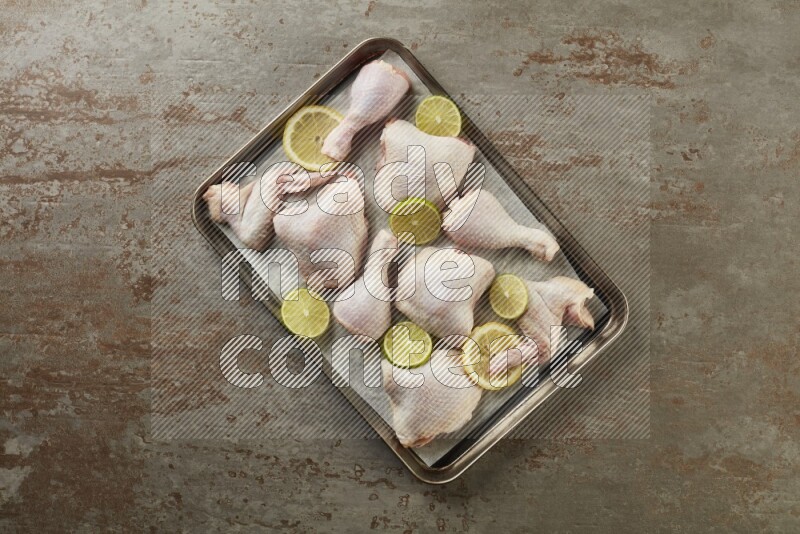 Mixed fresh chicken pieces in an oven tray on a textured rustic background