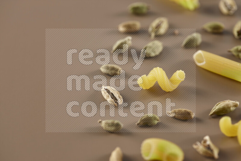 Raw pasta with different ingredients such as cherry tomatoes, garlic, onions, red chilis, black pepper, white pepper, bay laurel leaves, rosemary and cardamom on beige background