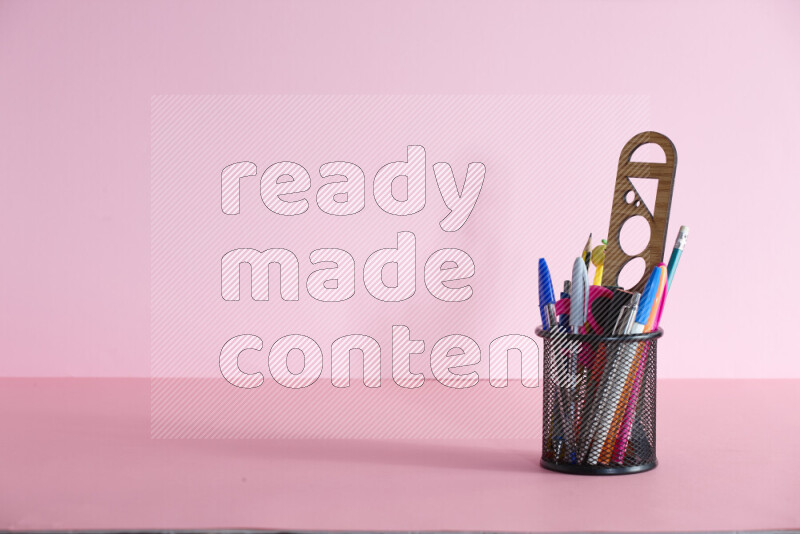 Pens, pencils and other different school supplies in a metal pen holder on rose background