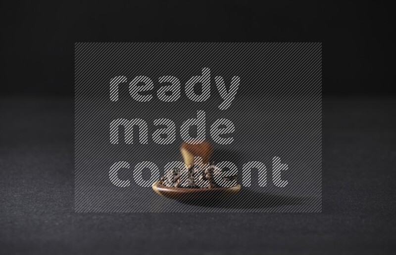 A wooden ladle full of whole cloves on a black flooring