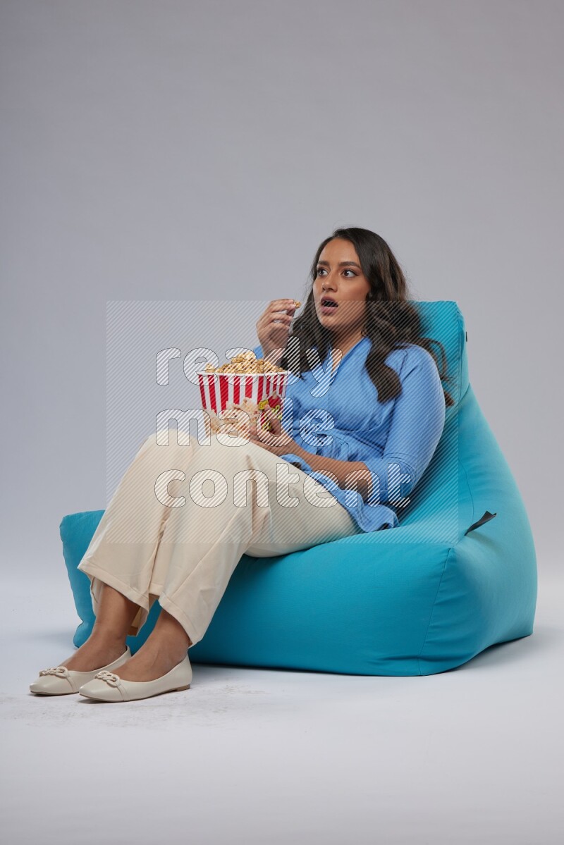 A woman sitting on a blue beanbag and eating popcorn
