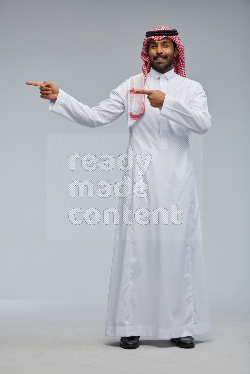 Saudi man Wearing Thob and shomag standing interacting with the camera on Gray background