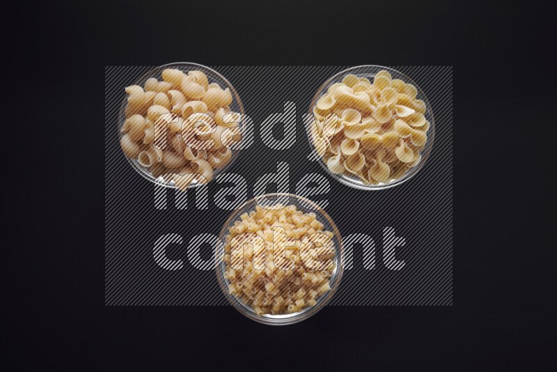 Different pasta types in glass bowls on black background