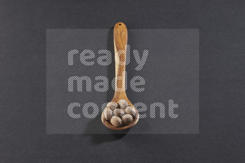 A wooden ladle full of whole nutmeg seeds on a black flooring