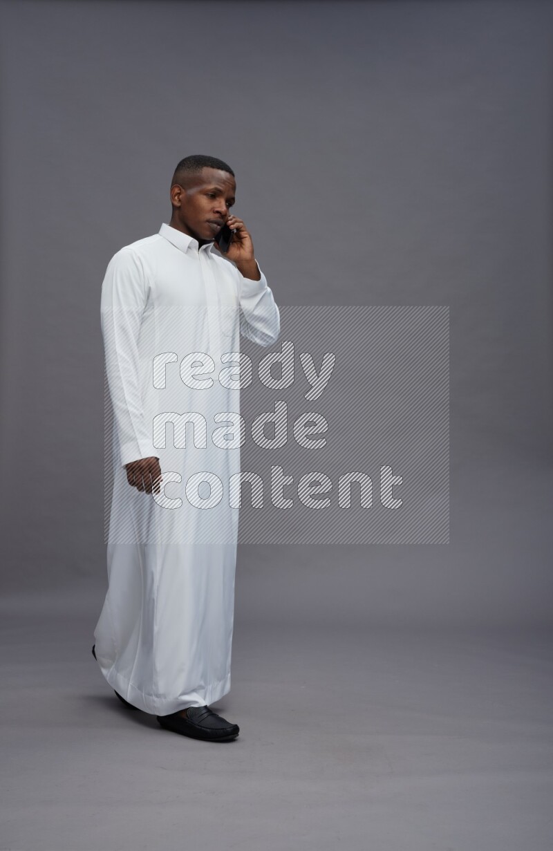 Saudi man wearing thob standing talking on phone on gray background