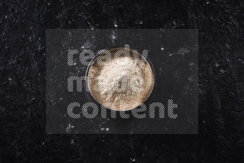 A black pottery bowl full of onion powder on black background