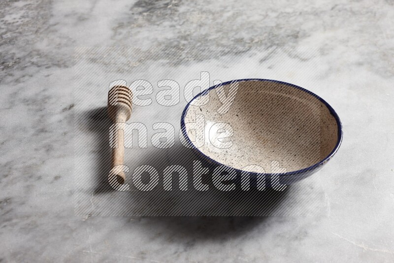 Multicolored pottery bowl with wooden honey dipper on the side on grey marble background