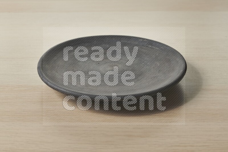 A circular black pottery plate on light wooden background