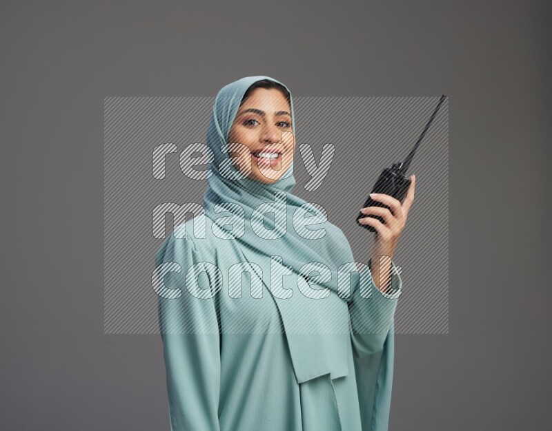 Saudi Woman wearing Abaya standing holding walkie-talkie on Gray background