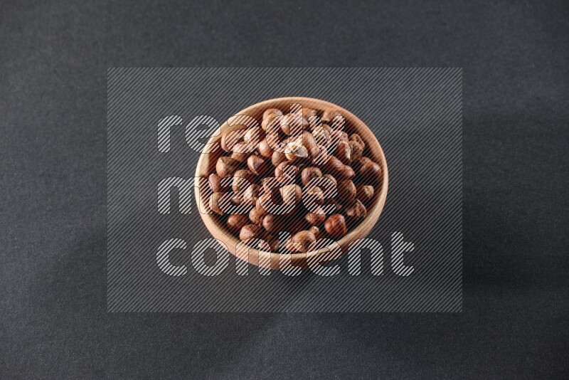 A wooden bowl full of peeled hazelnuts on a black background in different angles