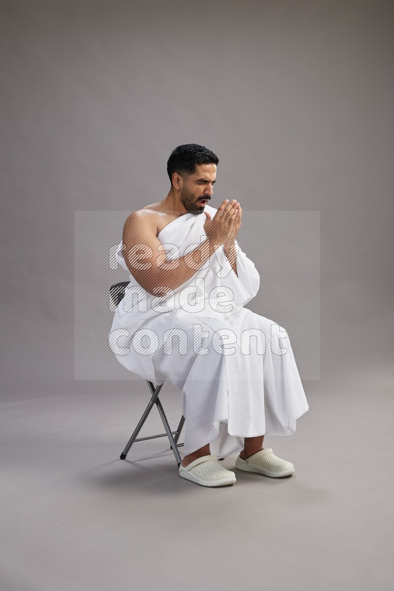 A man wearing Ehram sitting on chair showing how to sneeze on gray background
