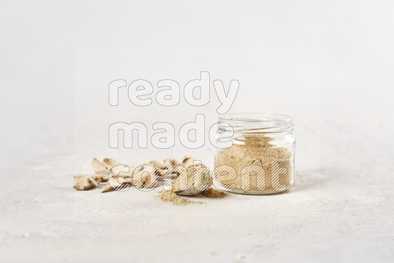 A glass jar full of ground ginger powder on white background
