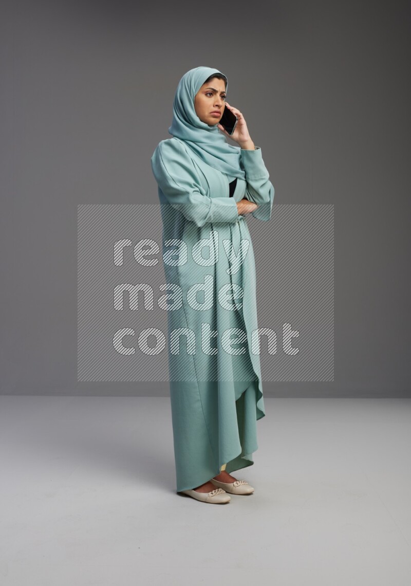 Saudi Woman wearing Abaya standing talking on phone on Gray background
