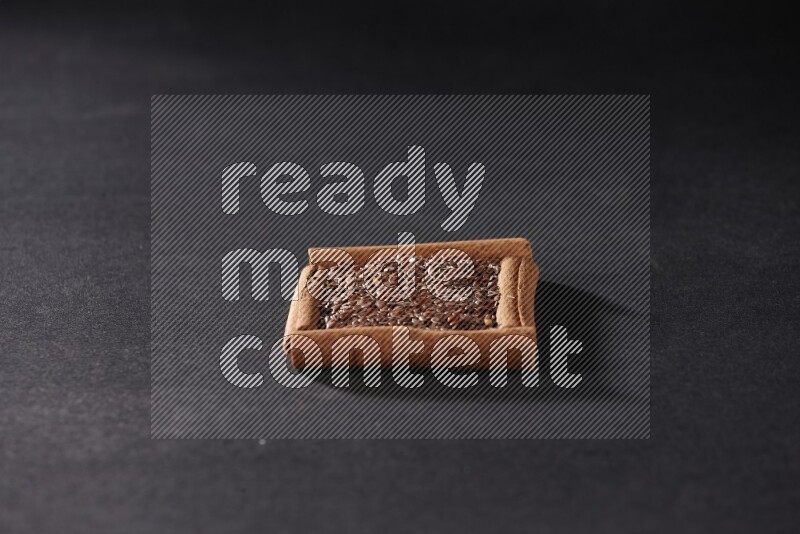 A single square of cinnamon sticks full of flaxseeds on black flooring