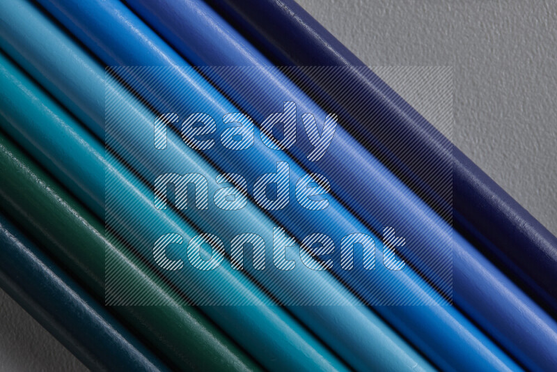 A collection of colored pencils arranged showcasing a gradient of blue hues on grey background