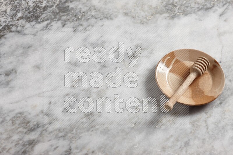 Multicolored pottery plate with wooden honey dipper in it on grey marble background