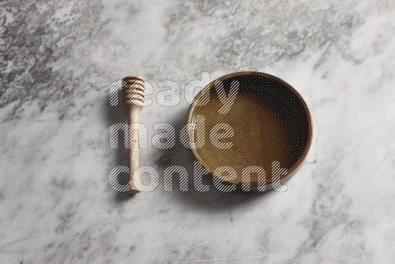 Multicolored pottery oven plate with wooden honey dipper on the side on grey marble background