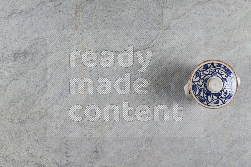 إناء فخاري متعدد الألوان مع غطائه على خلفية من الرخام الرمادي