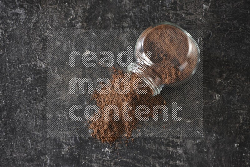 وعاء زجاجي للتوابل مقلوب ممتلئ ببودرة القرنفل والبودرة سقطت منه على أرضية سوداء