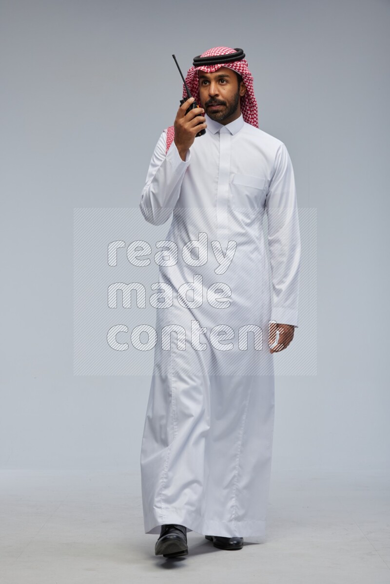Saudi man Wearing Thob and shomag standing holding walkie-talkie on Gray background