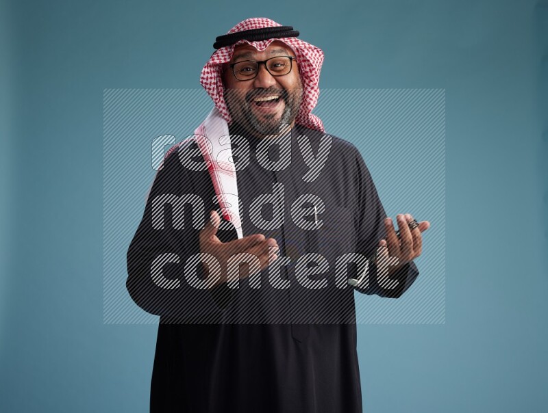 Saudi Man with shimag Standing Interacting with the camera on blue background