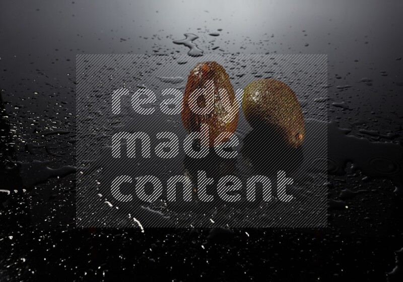 A whole avocado on black background with water drops.