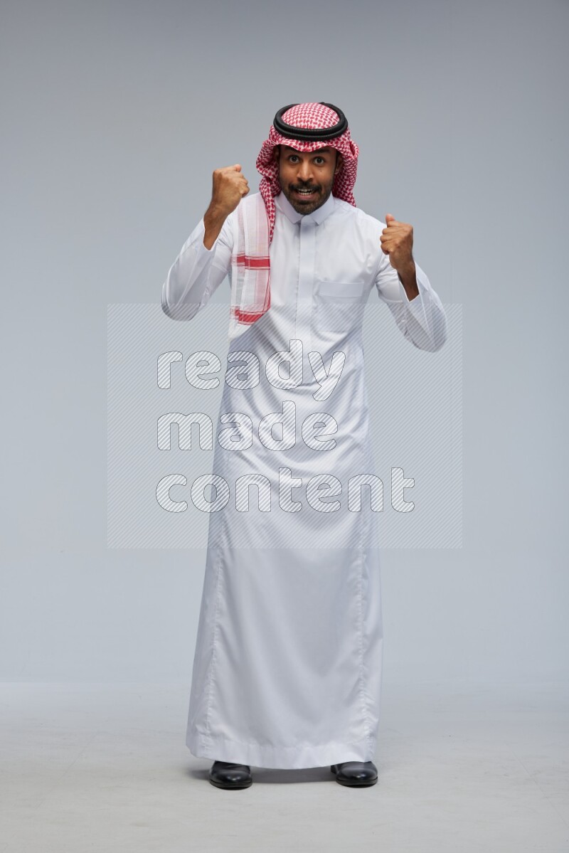 Saudi man Wearing Thob and shomag standing interacting with the camera on Gray background