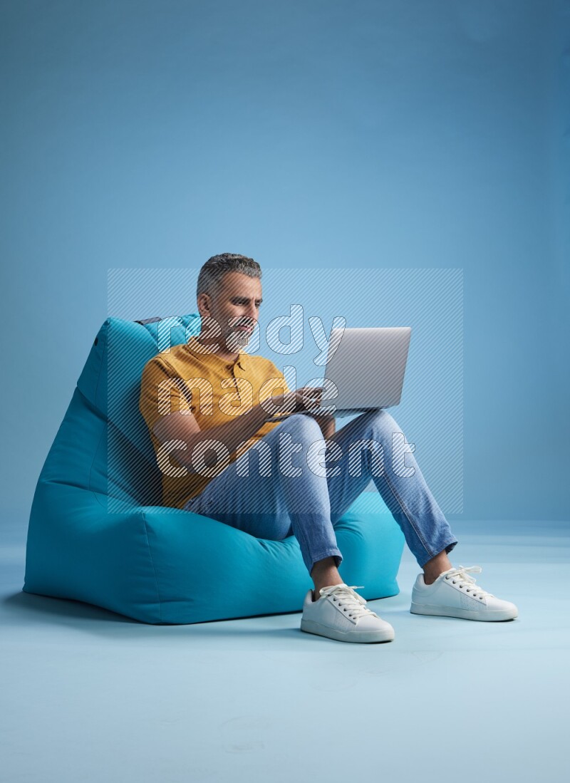 A man sitting on a blue beanbag and working on laptop