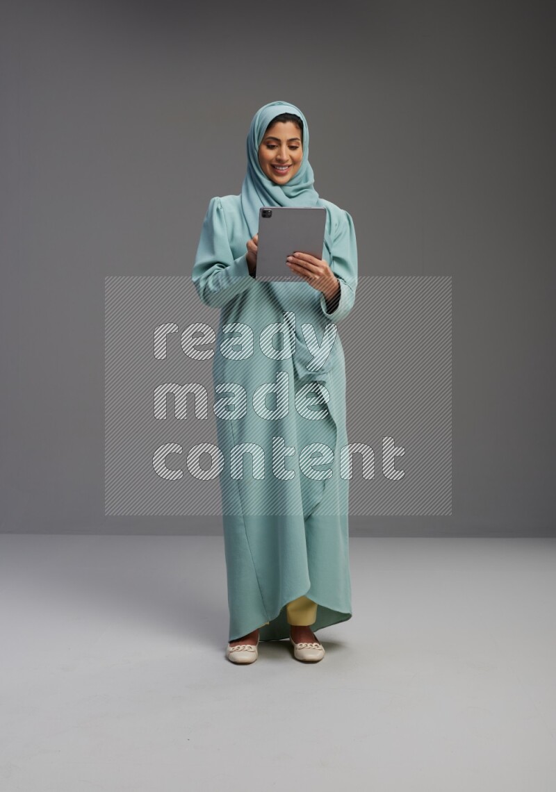 Saudi Woman wearing Abaya standing working on tablet on Gray background