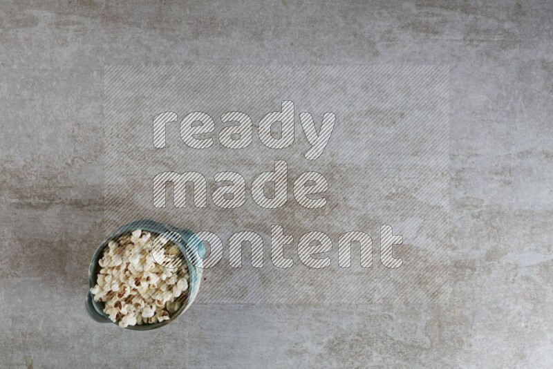 popcorn in a multi-colored handheld ceramic bowl on a grey textured countertop