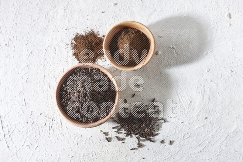 2 wooden bowls full of cloves powder and whole cloves on a textured white flooring
