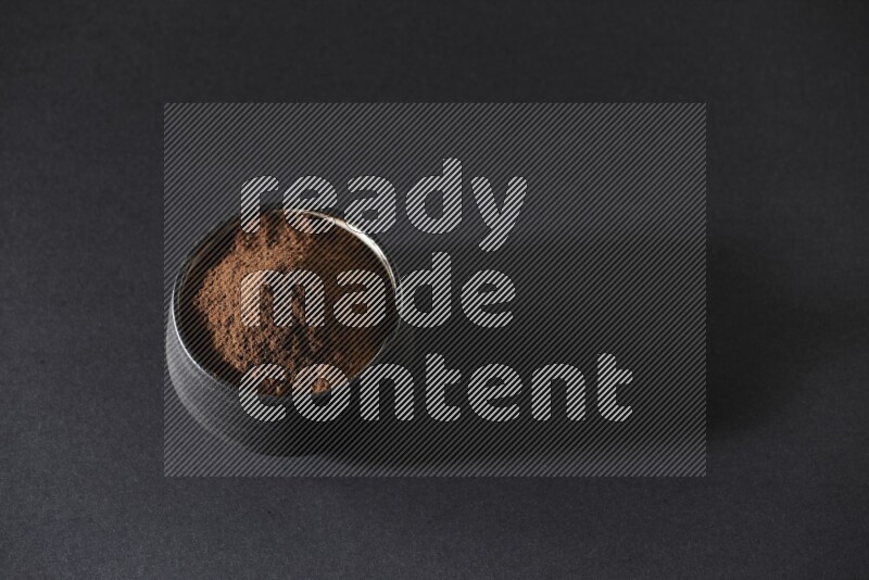 A black pottery bowl full of cloves powder on a black flooring