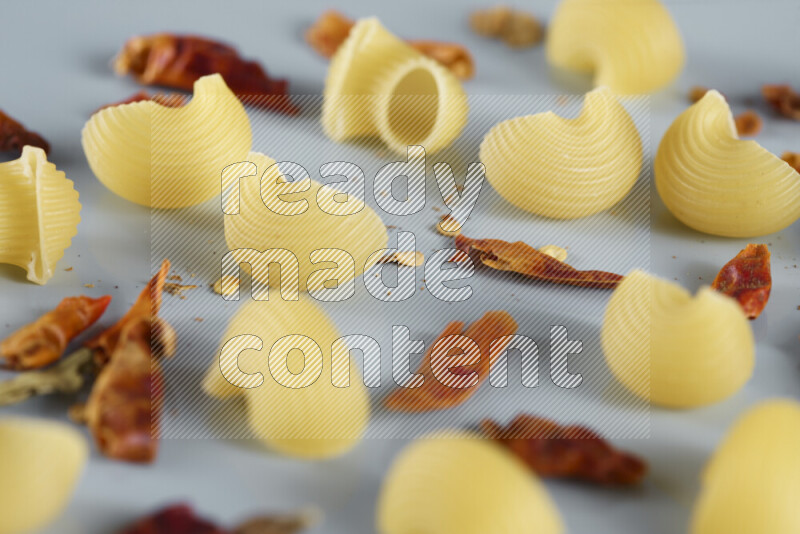Raw pasta with different ingredients such as cherry tomatoes, garlic, onions, red chilis, black pepper, white pepper, bay laurel leaves, rosemary, cardamom and mushrooms on light blue background