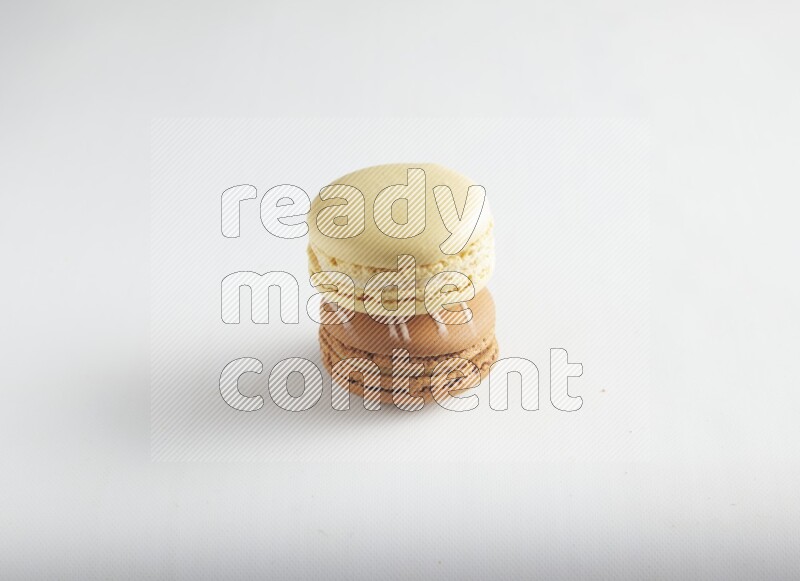 45º Shot of of two assorted Brown Irish Cream, and Yellow Vanilla macarons on white background