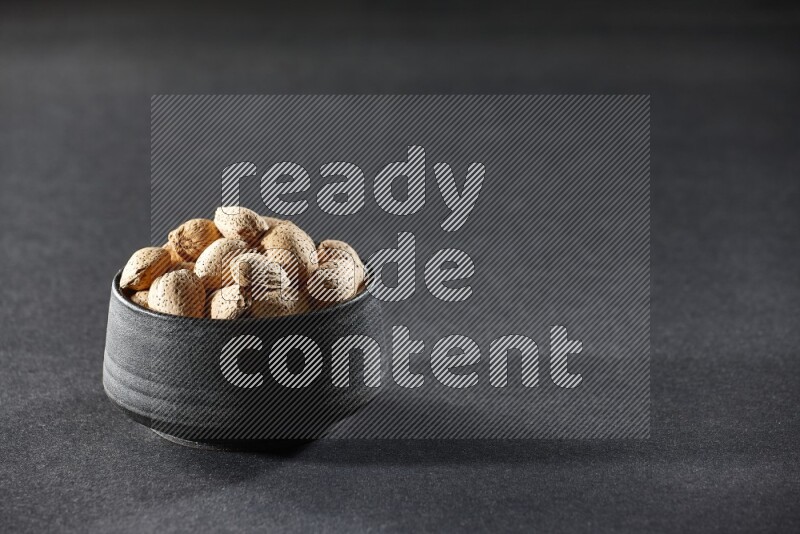 A black pottery bowl full of almonds on a black background in different angles