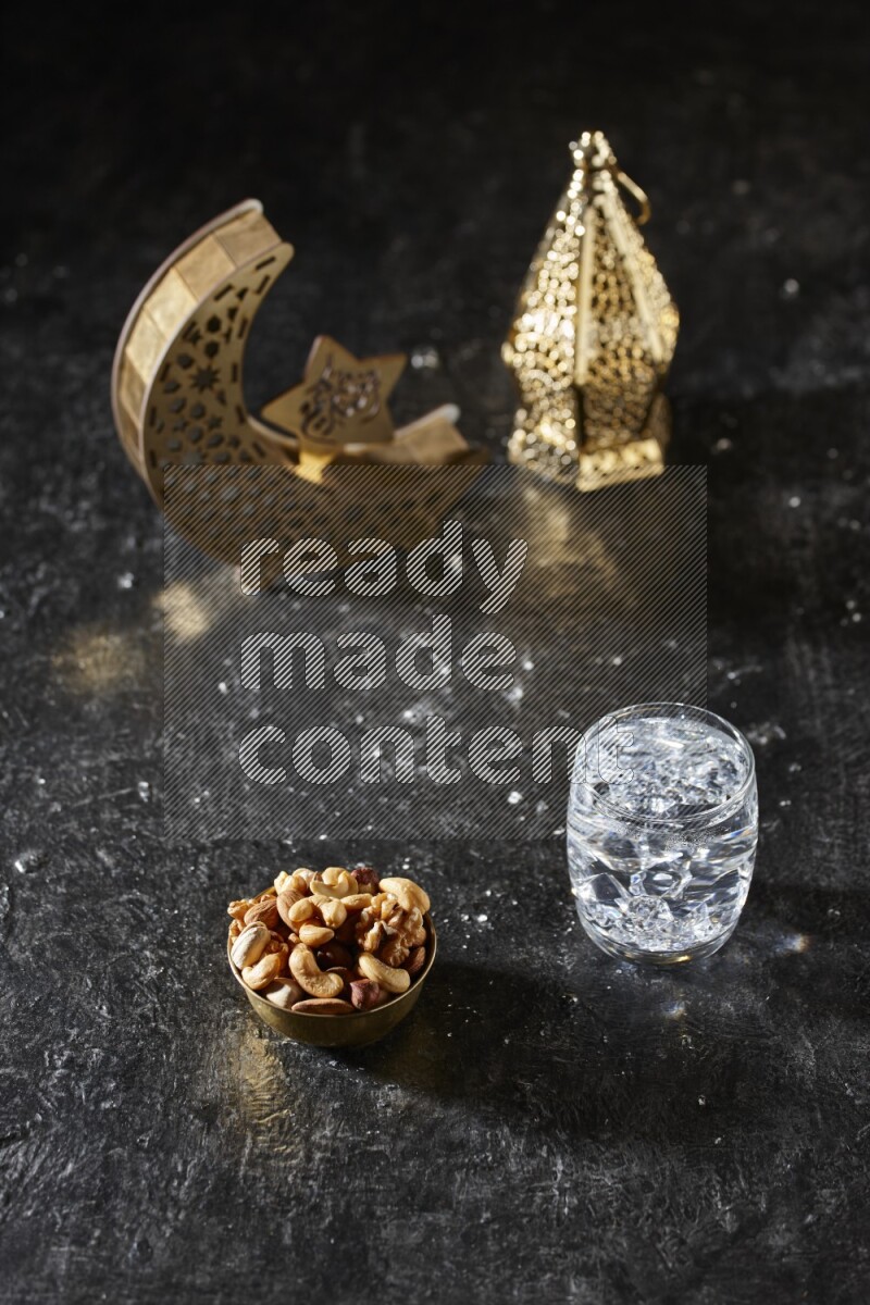 Nuts in a metal bowl with water beside golden lanterns in a dark setup