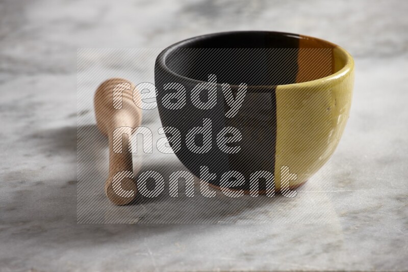 Multicolored pottery bowl with wooden honey dipper on the side on grey marble background