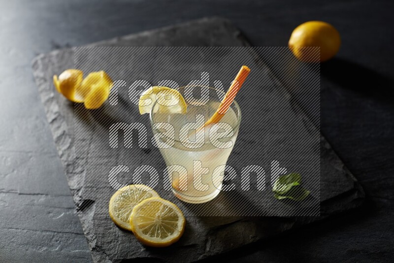 A glass of lemon juice with a straw on black background