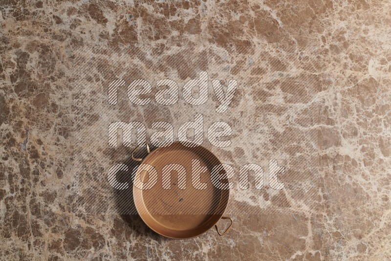 A small copper pan on beige marble background