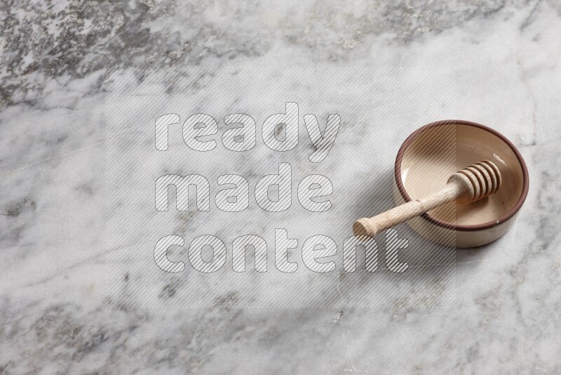 Beige Pottery oven bowl with wooden honey handle on the side with grey marble flooring, 65 degree angle