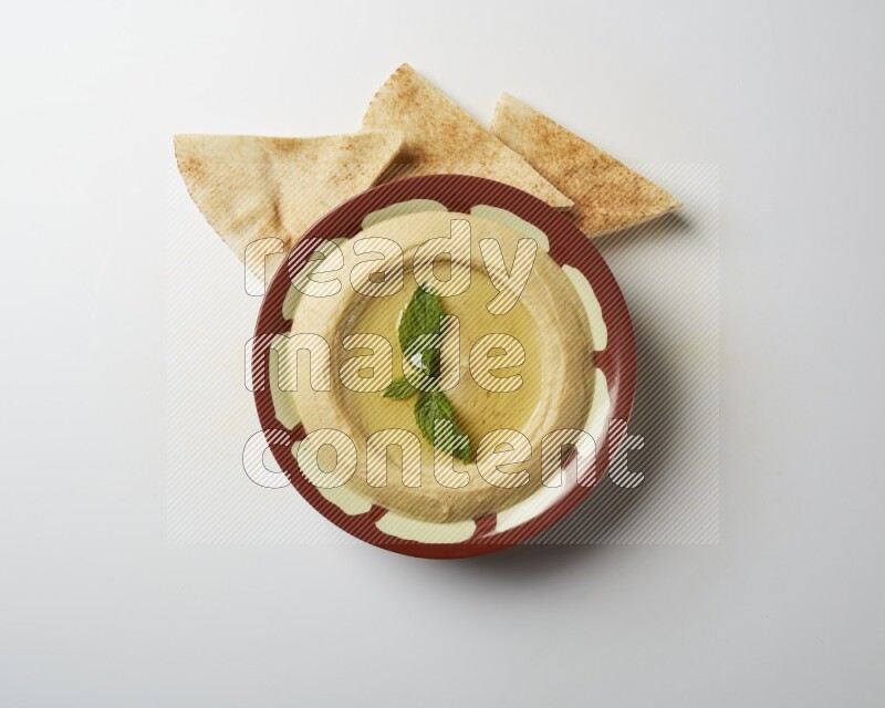 Hummus in a traditional plate garnished with mint on a white background
