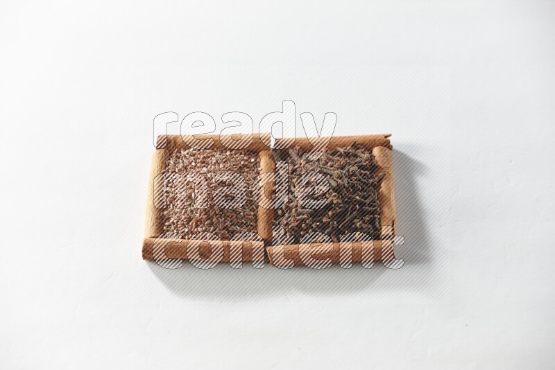 مربعان من أعواد القرفة ممتلئان بالقرنفل وبذور الكتان علي خلفية بيضاء