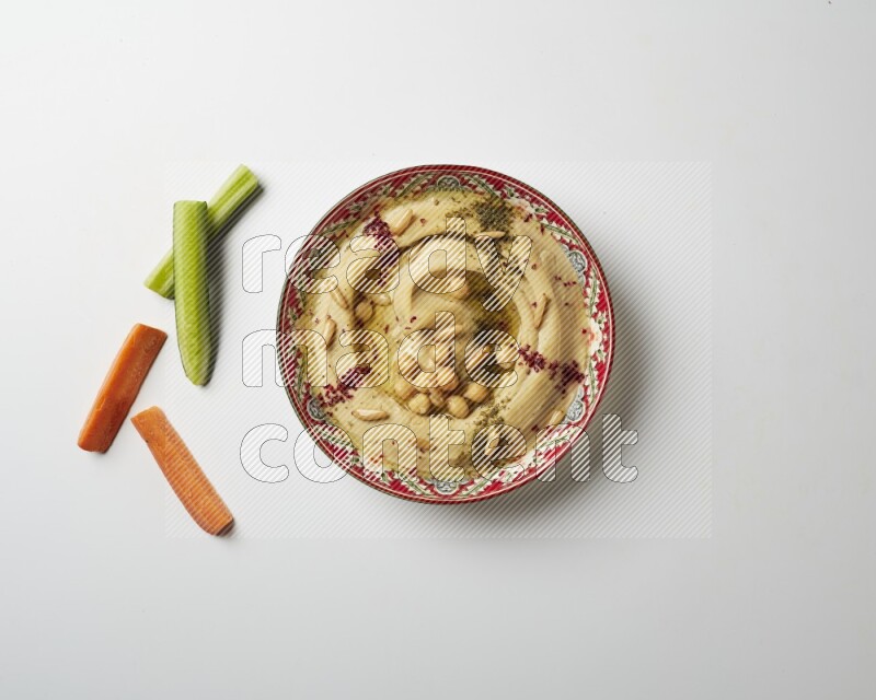 Hummus in a red plate with patterns garnished with zaatar & sumak on a white background